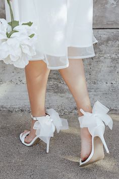 the bride's shoes are white with bows on them and they have flowers in them