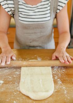 a woman rolling out dough on top of a wooden table with a rolling pin in front of her