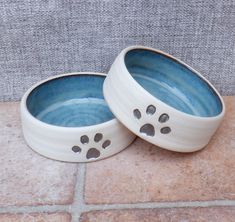 two ceramic bowls with paw prints on them sitting on a tile floor next to a wall