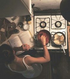 a woman is reading a book while cooking in the kitchen with an open cookbook