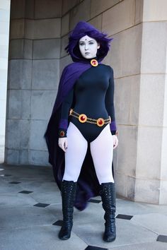 a woman dressed in a costume with purple hair and black boots, standing next to a wall