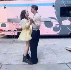 a man and woman standing in front of a pink bus with their hands around each other