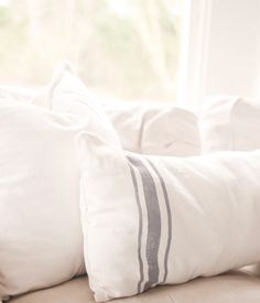 two white pillows sitting on top of a couch in front of a window with sunlight coming through the windowsill