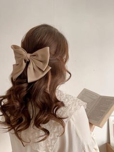 a woman with long hair wearing a bow in her hair and holding an open book