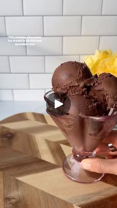 a person holding a glass filled with chocolate ice cream on top of a wooden table