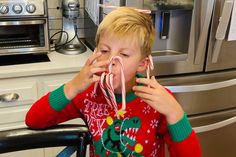 a young boy sitting at a kitchen table with candy in front of his face and an oven behind him