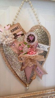 a heart shaped frame with flowers and ribbons hanging on the wall in front of a door