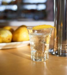 a glass filled with water sitting on top of a table next to some lemons