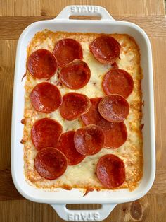 a pepperoni and cheese pizza in a white casserole dish on a wooden table