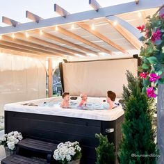 two children are sitting in an outdoor hot tub with lights on the roof above them