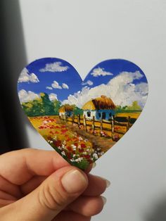 a hand holding up a heart shaped paper cutout with a farm scene in the background