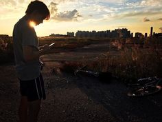 a person standing next to a bike on a dirt road with the sun setting in the background