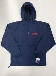 This NASA Champion half-zip packable jacket is a wind and rain resistant polyester jacket with a detailed NASA embroidery design. It has a practical hood, front kangaroo pocket, and zipped pouch pocket which you can pull out and use to scrunch the jacket into for convenient storage. This jacket ships separately directly from the supplier. Please allow 2-8 days from purchase date for order fulfillment. Color: Navy Product Details: • 100% polyester micro poplin • Wind and rain resistant • Half zip Hooded Camping Jacket With Pockets, Camping Hooded Jacket With Pockets, Hooded Jacket With Pockets For Camping, Fall Camping Windbreaker With Pockets, Nylon Half-zip Windbreaker With Adjustable Hood, Long Sleeve Hooded Jacket With Pockets For Camping, Long Sleeve Hooded Jacket For Camping, Hooded Windbreaker With Side Pockets For Travel, Long Sleeve Windbreaker With Pockets For Camping