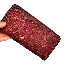 a hand holding a red leather wallet with intricate embossing on the front and sides