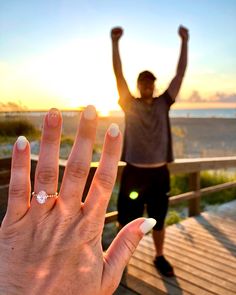 two people standing on a boardwalk with their hands in the air and one person raising their arms up