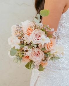 a woman in a wedding dress holding a bridal bouquet with peach and white flowers