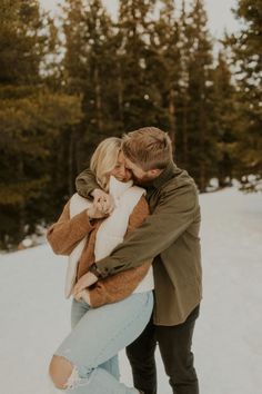 a man and woman hugging in the snow with trees in the backgrouds