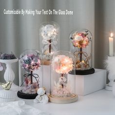 three snow globes filled with flowers on top of a white table next to candles