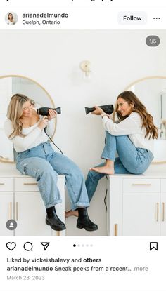 two women sitting on top of a white counter with hair dryers in their hands