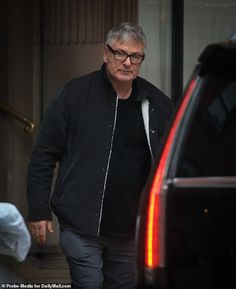 an older man in black jacket and glasses walking towards a car