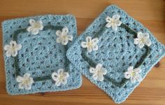 two square crocheted coasters with white flowers on them sitting on a table