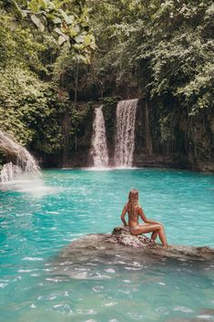 a woman sitting on top of a rock in front of a blue pool with waterfall