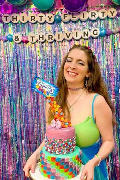 a woman holding a birthday cake in front of a party backdrop