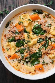 a white bowl filled with pasta and spinach soup on top of a wooden table