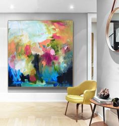 an abstract painting hangs on the wall next to a yellow chair