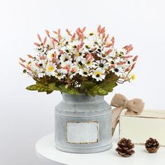 a vase filled with white flowers next to a small box and pine cones on a table