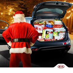 a man dressed as santa clause standing next to a car with presents in the trunk