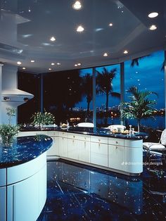 a kitchen with an island counter and large windows overlooking the ocean at night time,