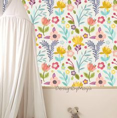 a white bed sitting next to a wall with flowers on it and a curtain hanging from the ceiling