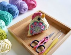 a crocheted bird sitting on top of a wooden tray next to scissors and yarn