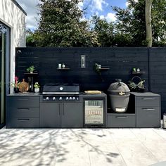 an outdoor kitchen with grill, sink and cabinets on the outside patio next to trees