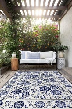 a blue and white area rug on a wooden deck with potted plants in the background