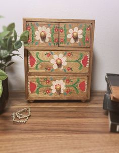 a wooden box with flowers painted on it next to a potted plant and other items