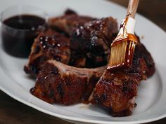 barbecue ribs on a white plate with bbq sauce being drizzled over them