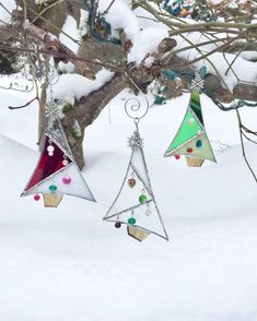 three glass christmas trees hanging from a tree branch in the snow with ornaments attached to them