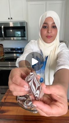 a woman in a hijab is holding up some kind of chocolate item on a wooden table