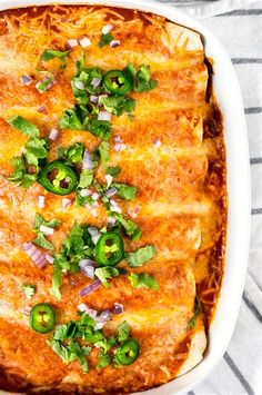 an enchilada casserole in a white dish with green peppers and onions