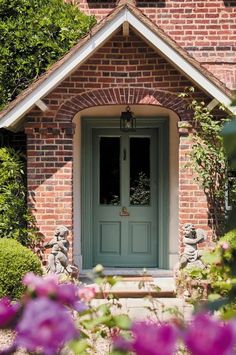 a green door in front of a red brick house with purple flowers around the doorway