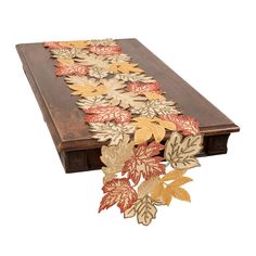 a wooden table topped with leaves on top of a white background and an orange, yellow, and red runner