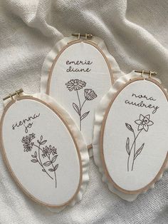 three embroidered hoop frames with flowers and words written on them, sitting on a white cloth