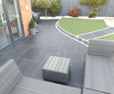 an outdoor patio area with grey wicker furniture and green grass on the side walk