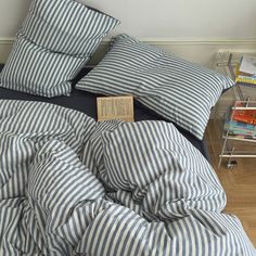 there is a bed with blue and white striped sheets on it, next to a bookshelf