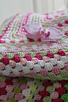 a crocheted blanket with a pink flower on the top and green, white, and pink squares around it