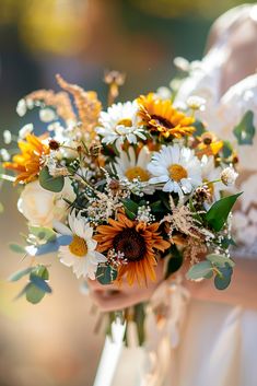 a bride holding a bouquet of sunflowers and greenery