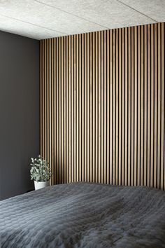 a bed with a black comforter next to a wooden paneled wall and potted plant