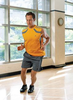 a man in an orange shirt is kicking a soccer ball on a hard wood floor